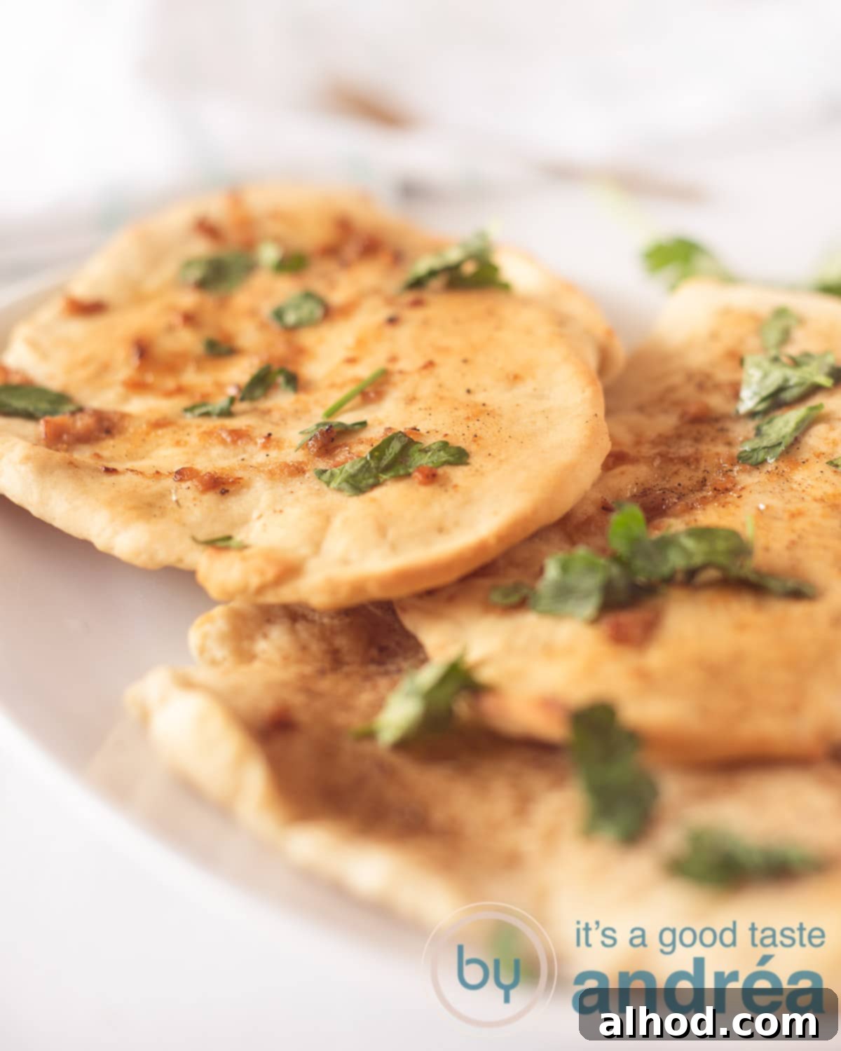 Buttery Garlic Herb Naan 5 An elevation photo showing a white bowl of three naans sprinkled with parsley. A white background.