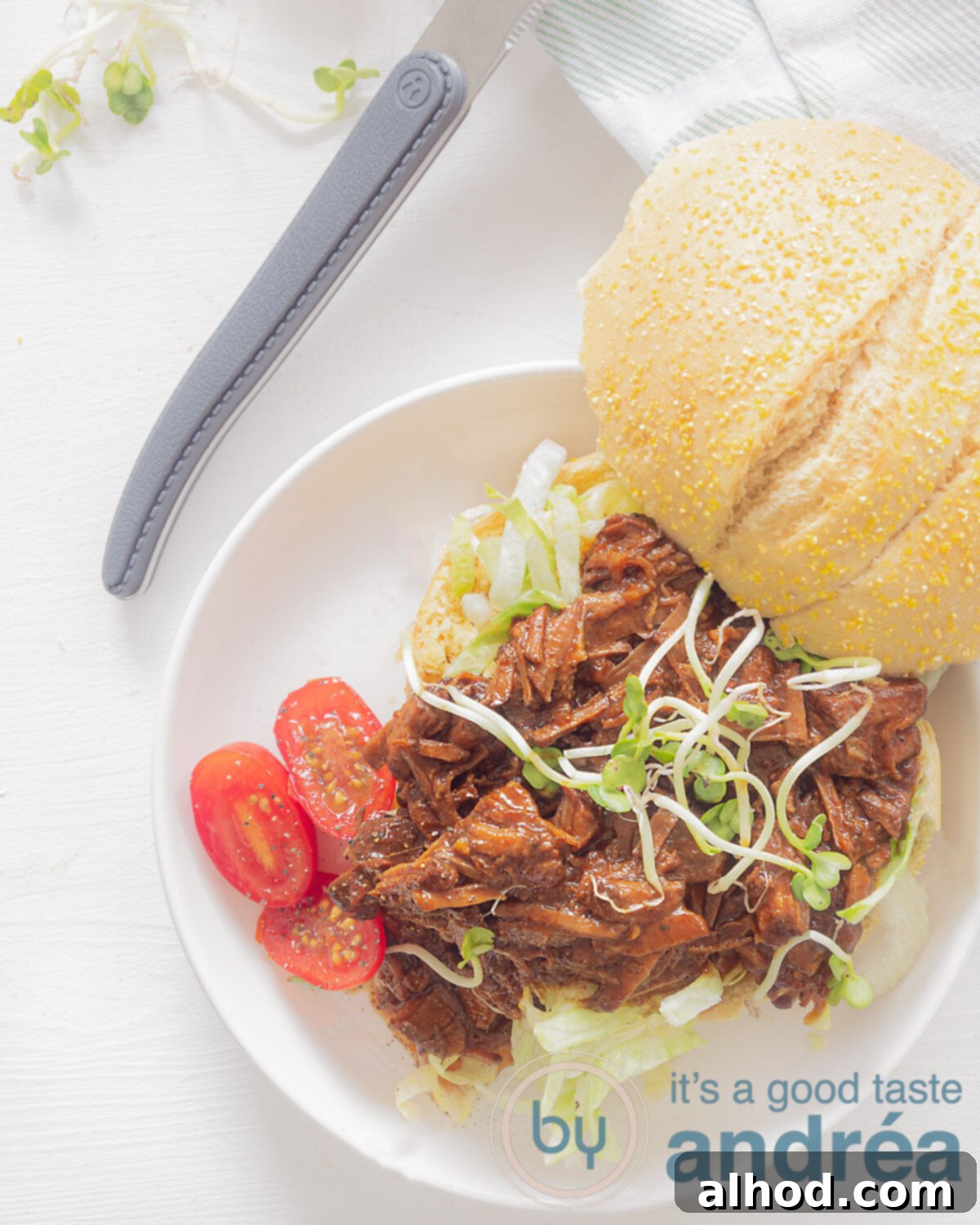 Sticky Asian Slow Cooker Beef 2 A photo from above of a sandwich with shredded beef, tomatoes and cress on it. A white background. A knife with a gray handle at the top