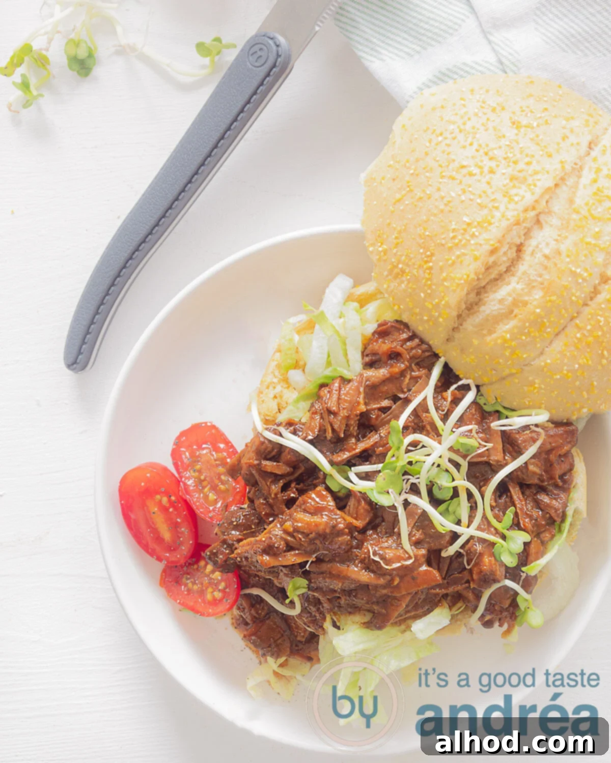 Umami-Rich Asian Slow Cooker Beef 2 A photo from above of a sandwich with shredded beef, tomatoes and cress on it. A white background. A knife with a gray handle at the top