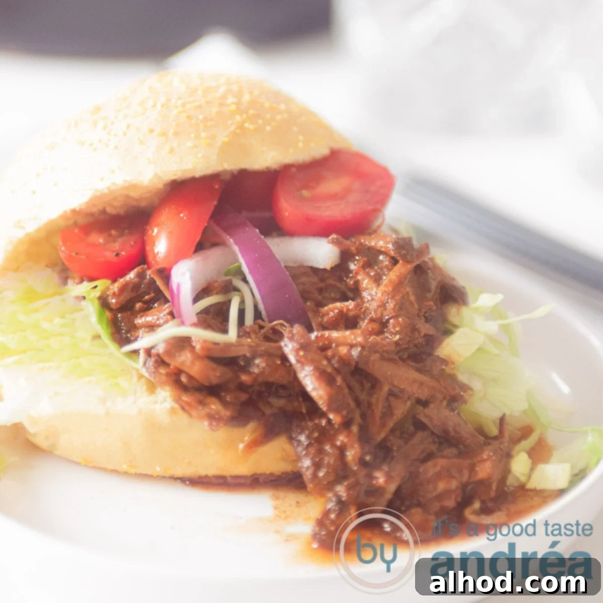Sticky Asian Slow Cooker Beef 6 A square photo with a corn ball filled with pulled beef, tomatoes, onion and lettuce. On a white plate on a white background