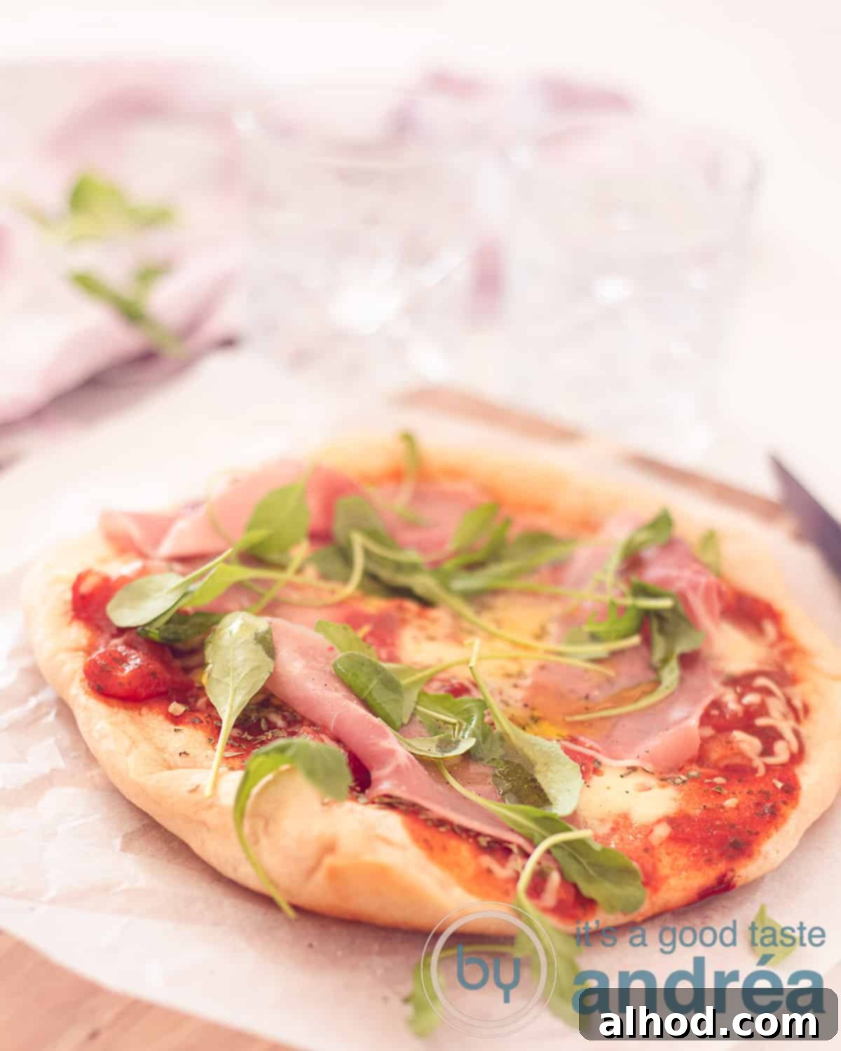 Homemade Pan Pizza: Foolproof Perfection Every Time 2 An aerial view with a pizza made in the frying pan and topped with tomato sauce, cheese, arugula and ham. On a baking paper on a wooden board.