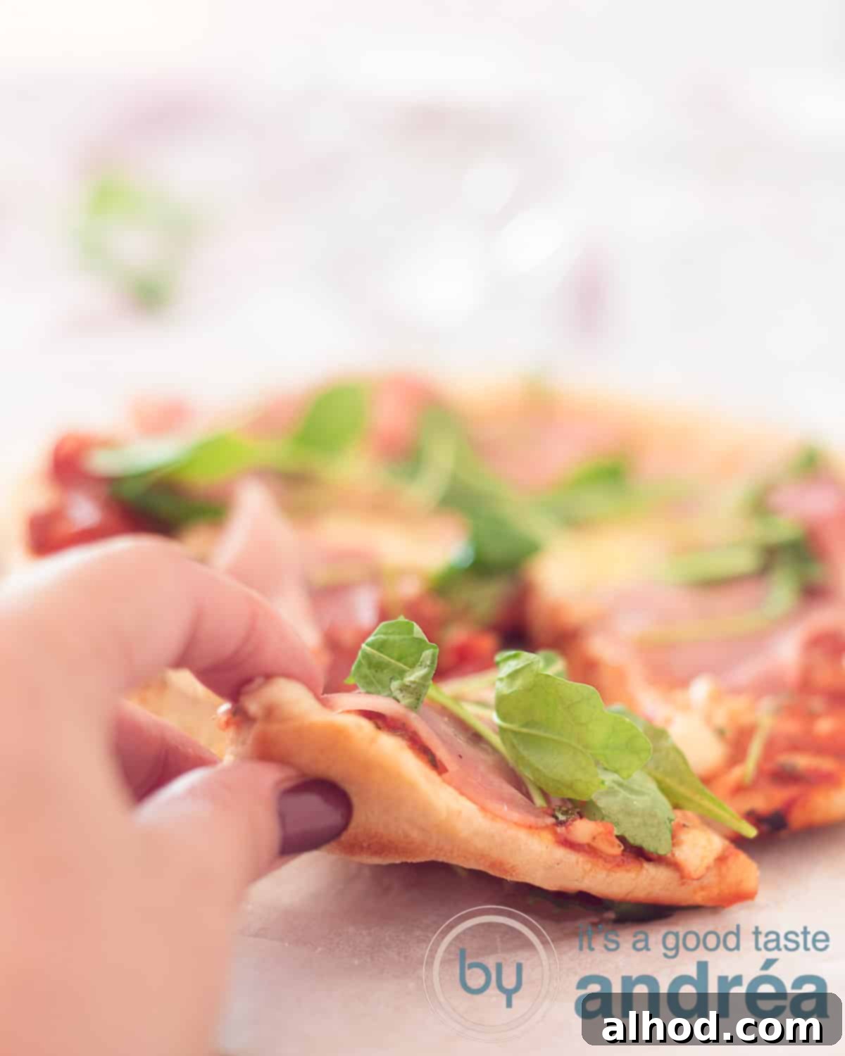 Homemade Pan Pizza: Foolproof Perfection Every Time 7 A picture of a pizza a slice cut of and is taken by a hand. Topped with arugula and cured ham.