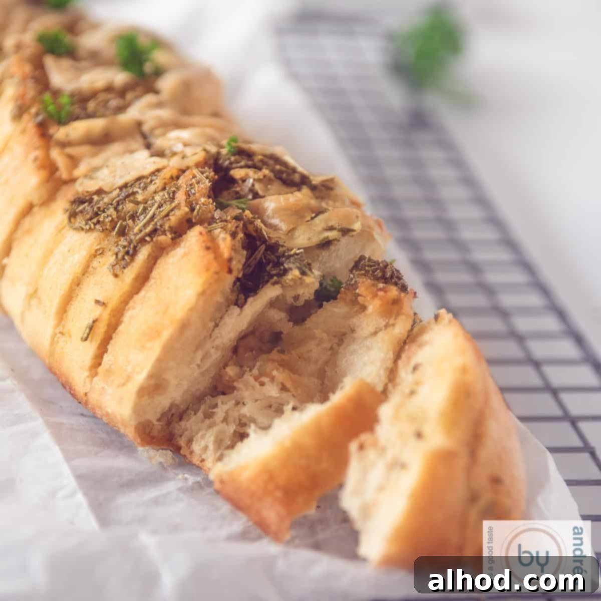 Herbed Garlic Baguette 4 A square photo with a baguette on a baking sheet, with two slices cut off and the garlic oil and herbs visible.