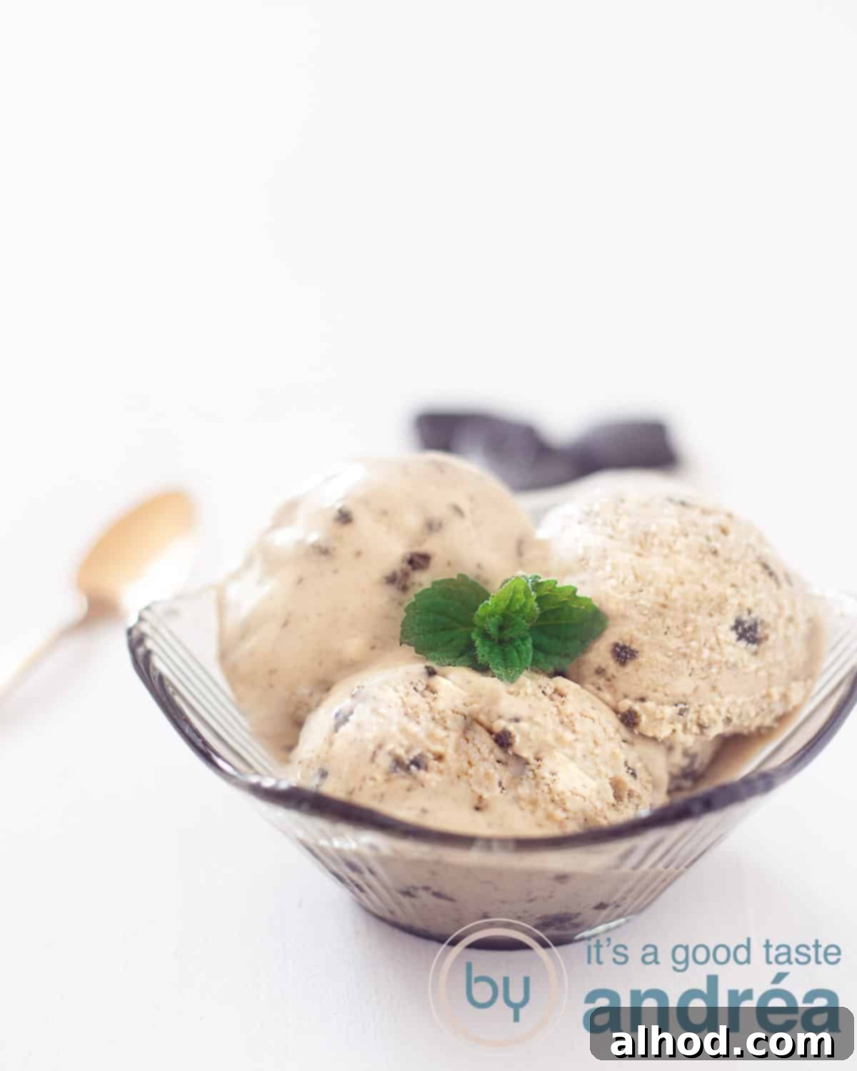 No-Churn Dutch Licorice Delight 2 A beautiful bowl filled with creamy, dark licorice ice cream, garnished with fresh mint leaves. A hand is scooping a generous portion.
