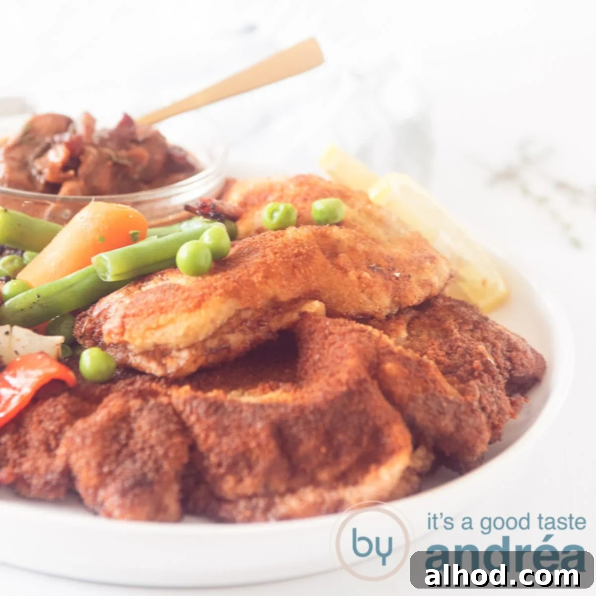 Easy German Jägerschnitzel 5 A square photo of a white plate with two schnitzels, vegetables and in the background a bowl with hunting sauce. A white background.
