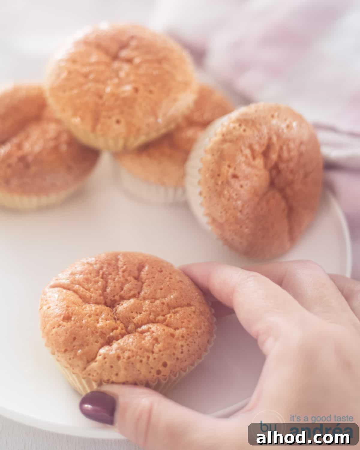 Creamy Milk Cupcakes 2 A white plate with a sweet milk cupcake being held in the foreground and four cupcakes in the background. The cupcakes are light golden brown and look incredibly moist, with a soft texture.
