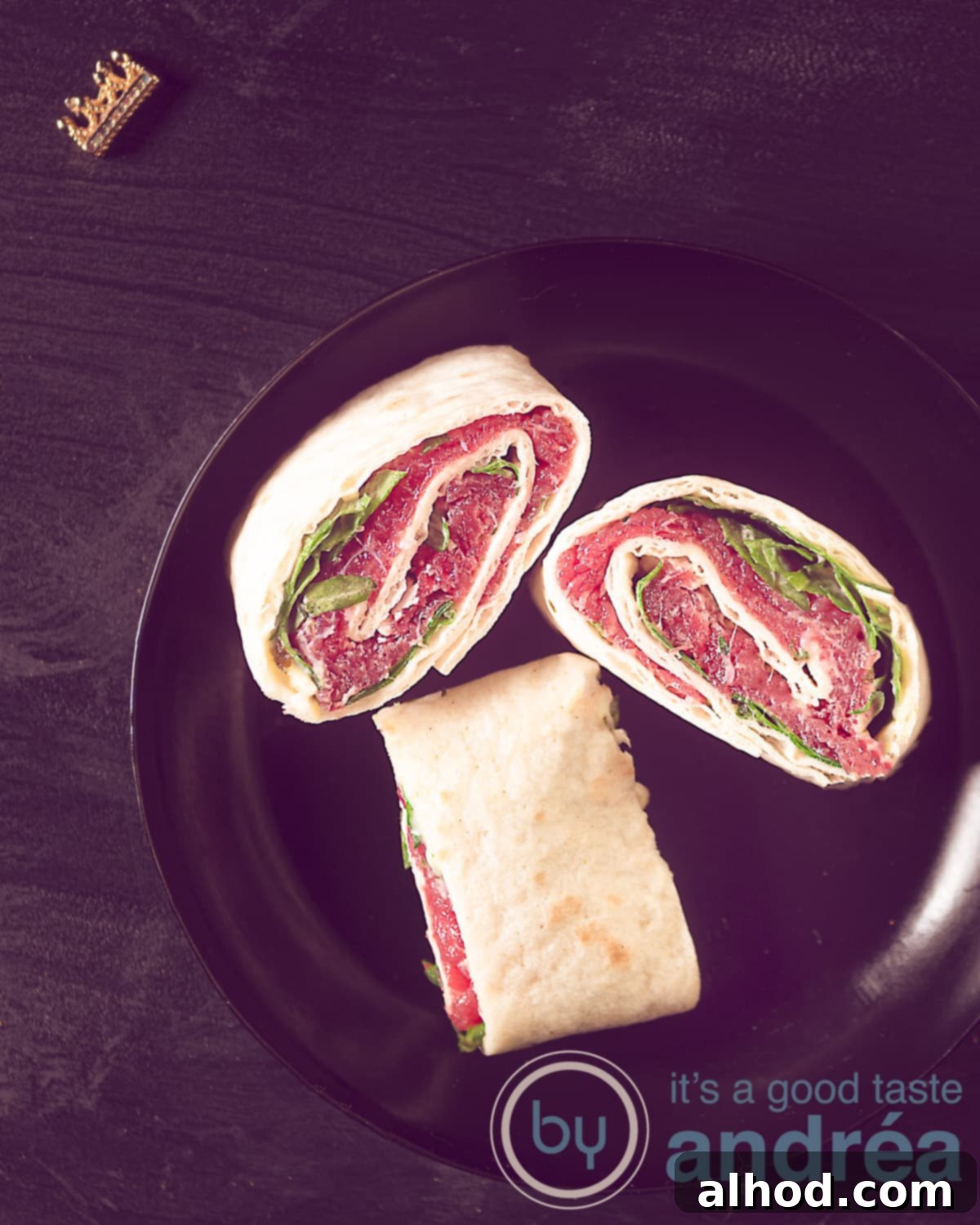 Classic Beef Carpaccio Pinwheels 5 An elevation photo of a black background with a black plate with three wraps with carpaccio, parmesan cheese and Heksenkaas.