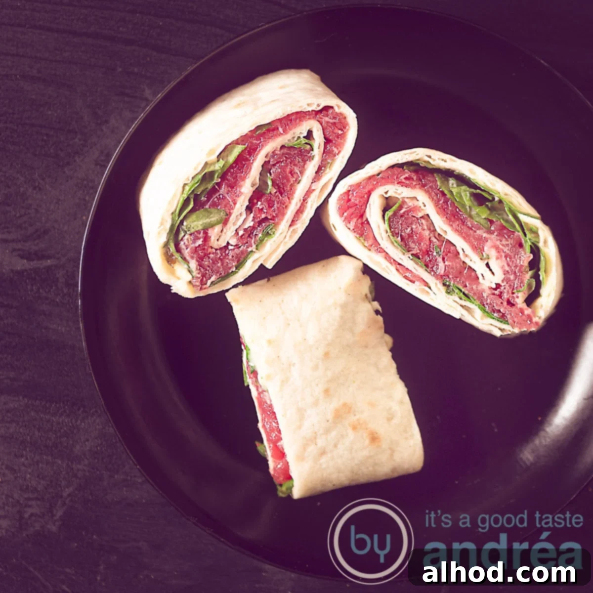 Classic Beef Carpaccio Pinwheels 6 A square photo of a black background with a black plate with three tortilla snacks filled with carpaccio, arugula, parmesan cheese.