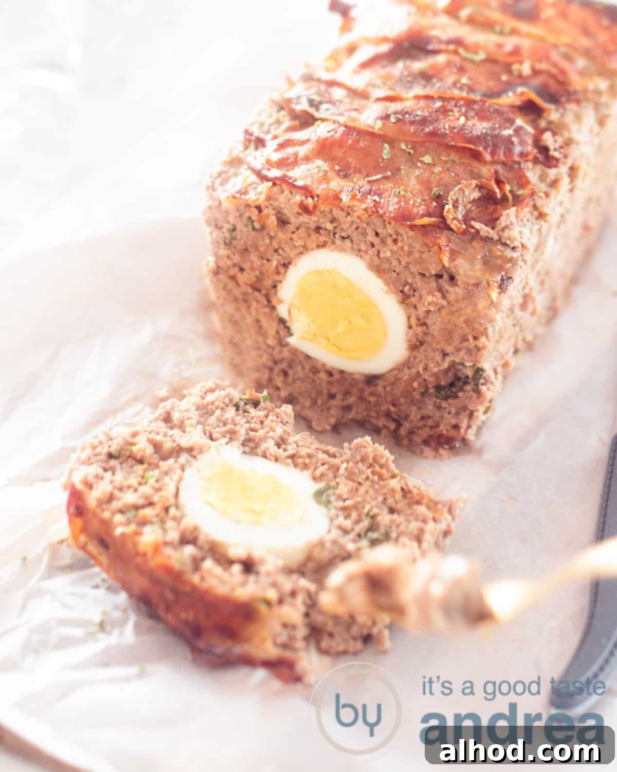 German Mock Hare Meatloaf 5 A height foot of a German meatloaf with one slice cut off. It is filled with egg and has a baking topping. A white background.