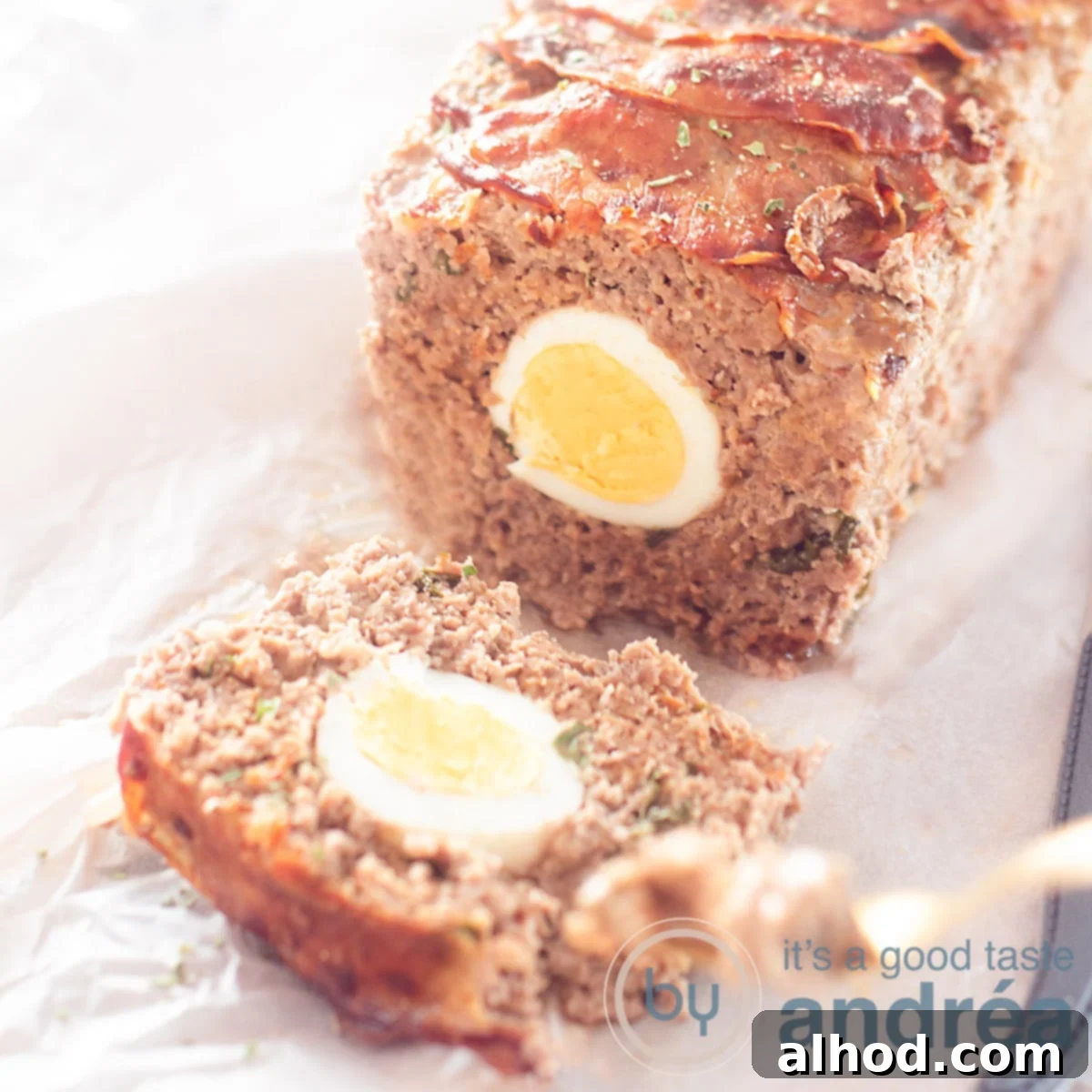 German Mock Hare Meatloaf 6 A square photo with meatloaf filled with egg and herbs on a baking paper. A golden fork takes a bite.