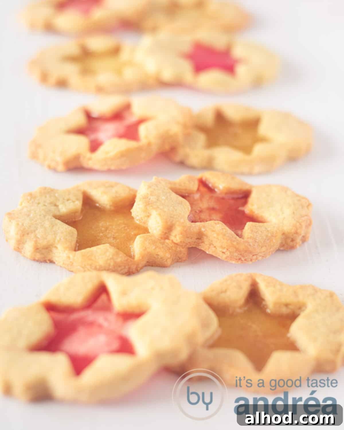 Jeweled Window Cookies 5 An elegant elevated photo showcasing eight pairs of vibrant stained glass biscuits, each with eye-catching red and yellow candy fillings, arranged artfully on a white background.