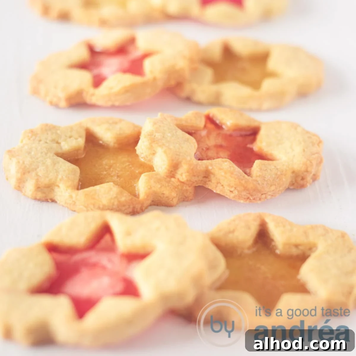Jeweled Window Cookies 6 A square photo featuring six beautiful cookies, each filled with colorful candies that create a stained glass effect. They are arranged in pairs (with red and yellow fillings) stacked on top of each other against a clean white background.