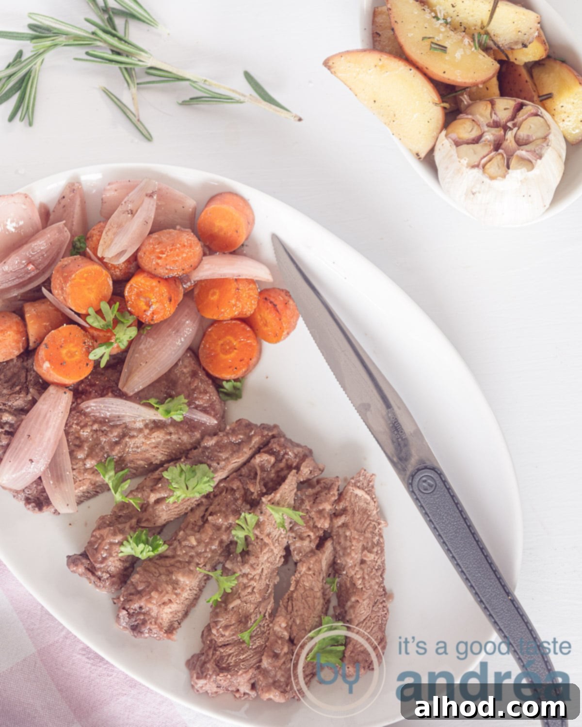 Succulent Roasted Sirloin with Deep Red Wine Sauce 2 A stunning overhead view of roasted sirloin steak served in a white bowl with a steak knife, accompanied by tender carrots and shallots. To the top left, golden roasted potatoes with garlic complete this exquisite meal.