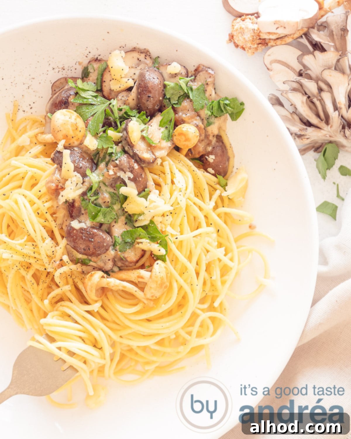 Luscious Creamy Garlic Mushroom Pasta 2 A photo from above with a mix of fresh mushrooms in the top right corner. On the left a white plate with spaghetti, fried mushrooms in a cream sauce, garnished with fresh parsley and grated cheese.