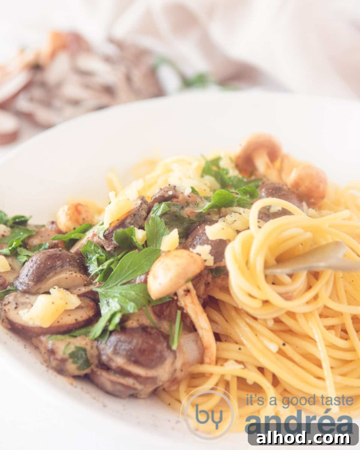 Luscious Creamy Garlic Mushroom Pasta 5 Part of a white plate with spaghetti, mushroom mix and cream sauce. A fork rolls some spaghetti.