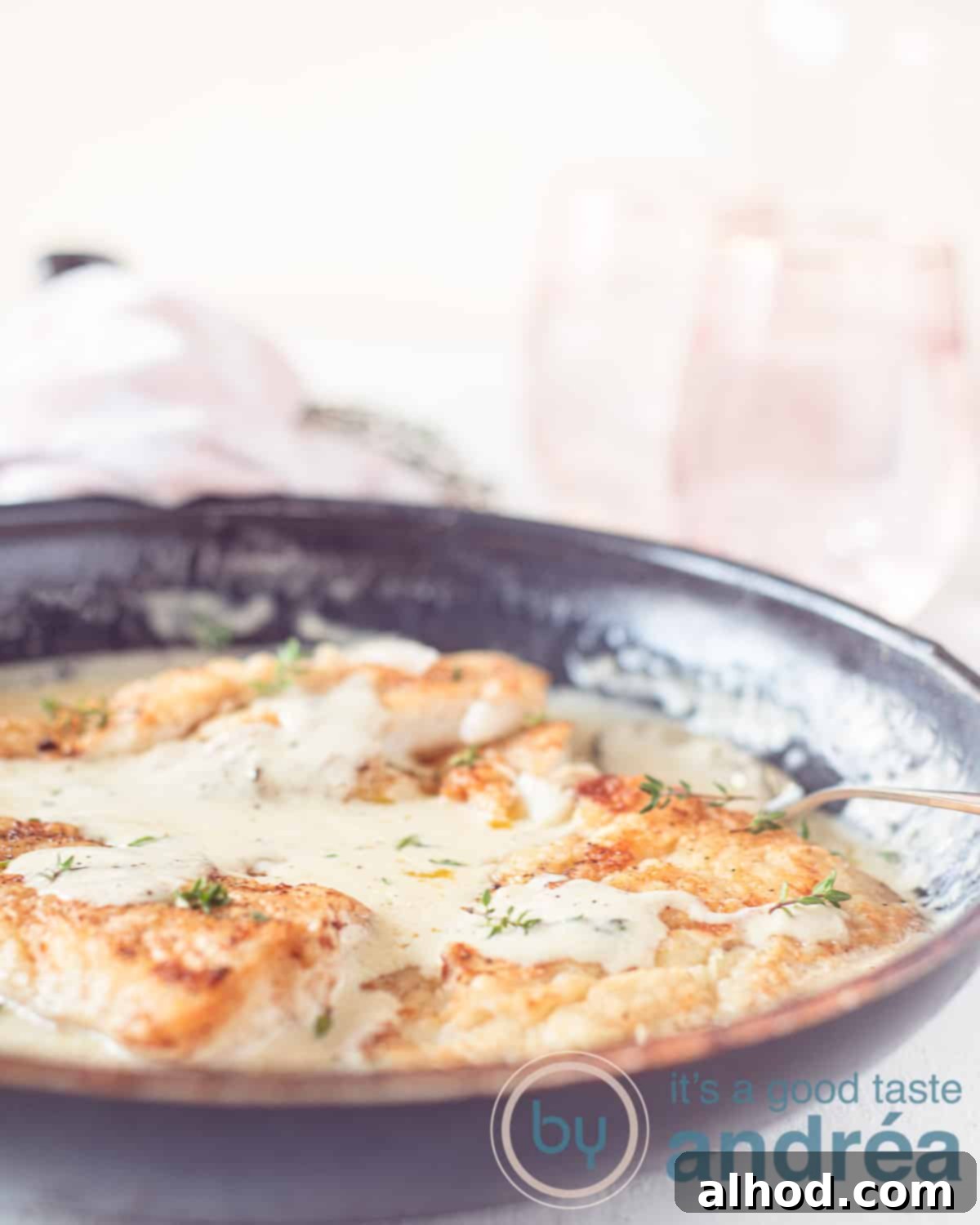 Cod Vin Blanc 2 A black frying pan filled with three cod fillets bathed in a creamy white wine lemon sauce, ready to serve on a white background.