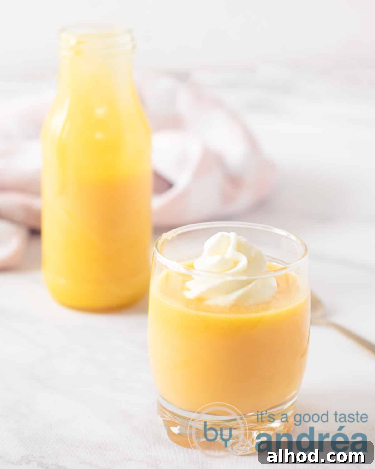 Advocaat Holland's Velvety Egg Liqueur 5 An elevation photo with a glass of eggnog, Dutch eggnog, with a dollop of whipped cream. Left behind a bottle from which lawyer has been poured. A pink white tea towel in the background.