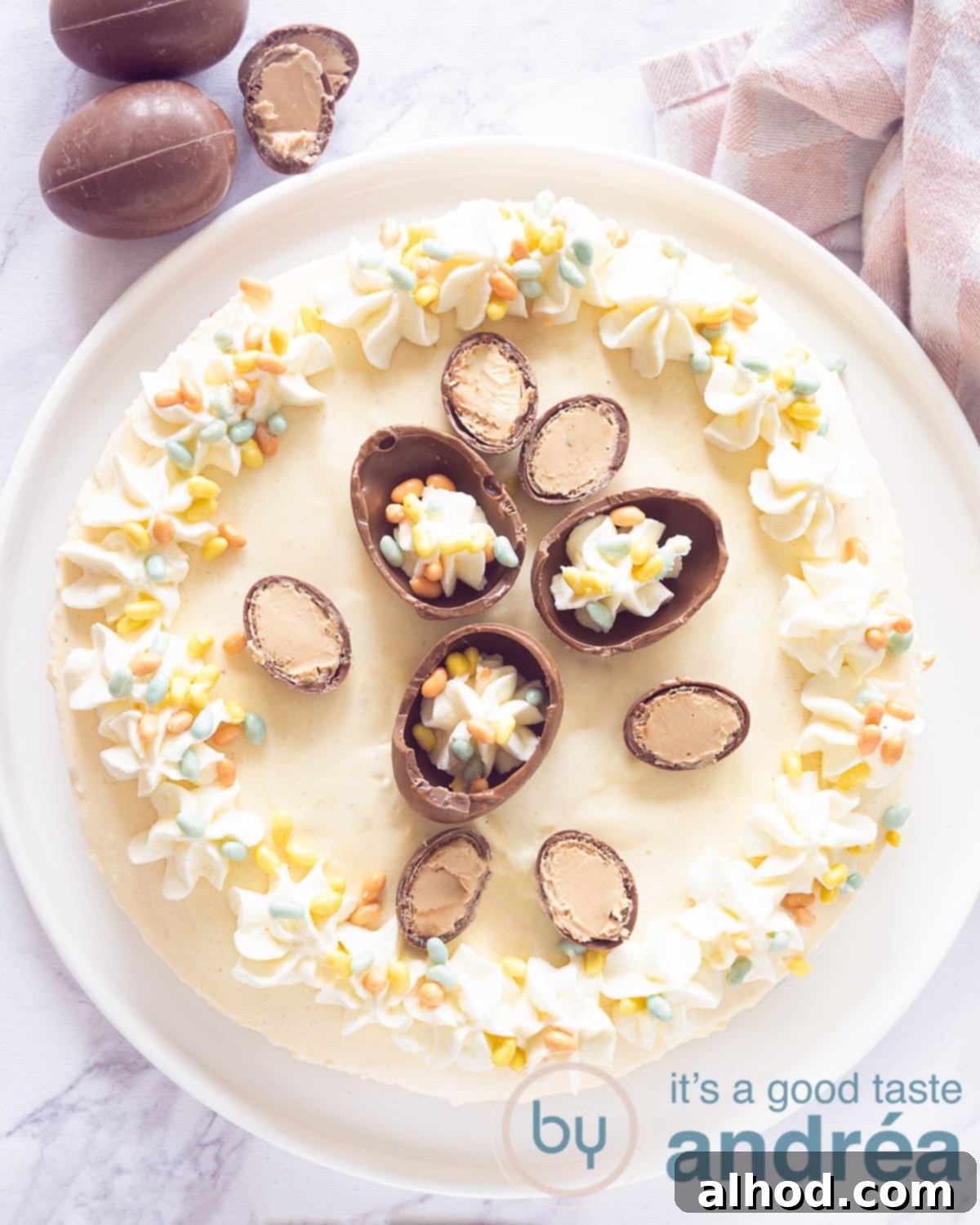 A photo from above of a no-bake cheesecake with eggnog, beautifully decorated with chocolate Easter eggs and generous swirls of whipped cream.