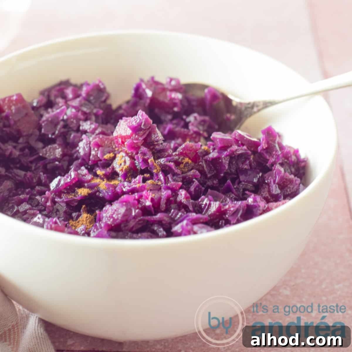 Ruby Red Balsamic Apple Braise 6 A square photo of a white bowl almost completely filled with red cabbage with apples and balsamic vinegar. A pink background.