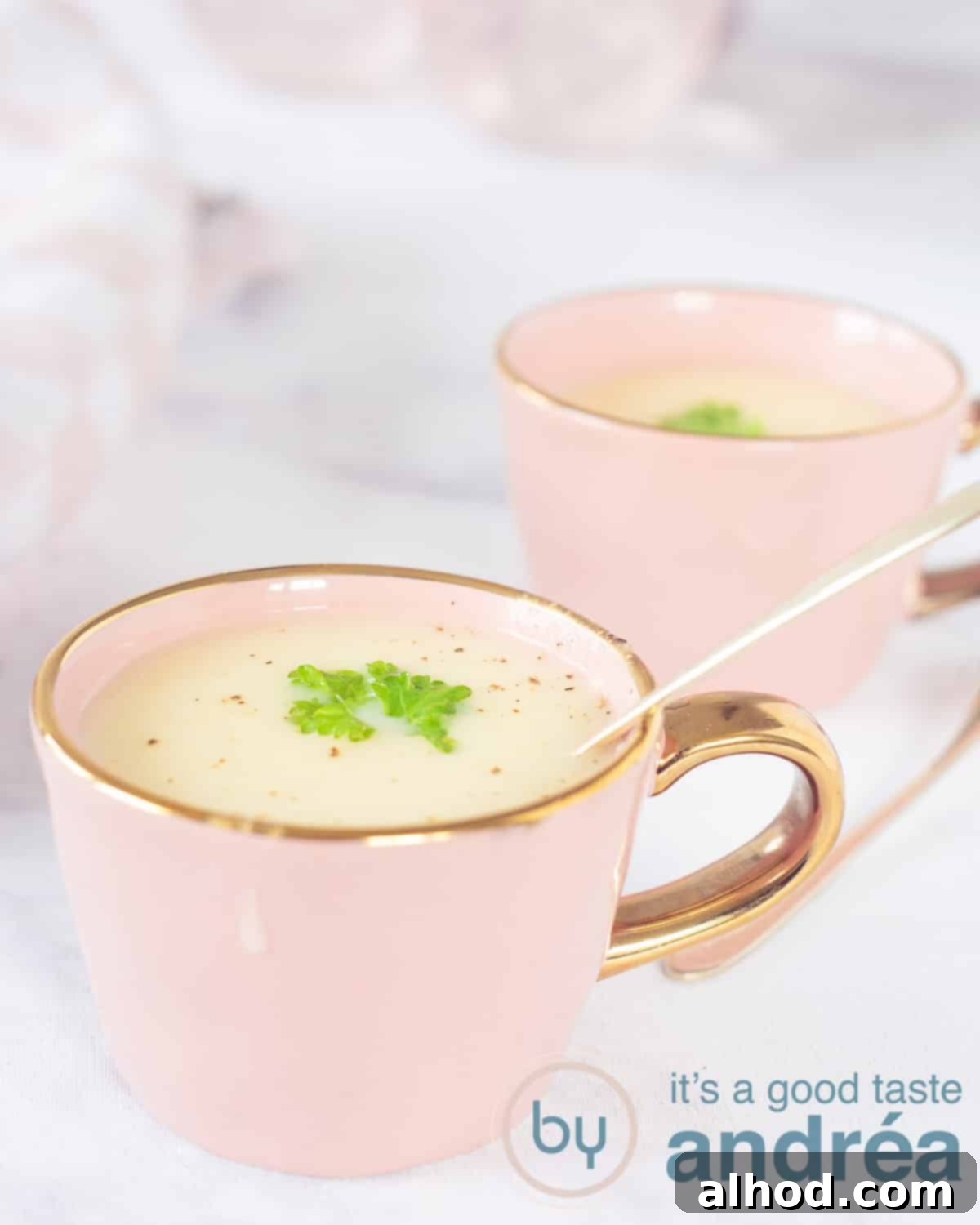 Velvety Asparagus Soup 5 Two pink cups filled with easy asparagus soup with a garnish of parsley. A marbled surface.