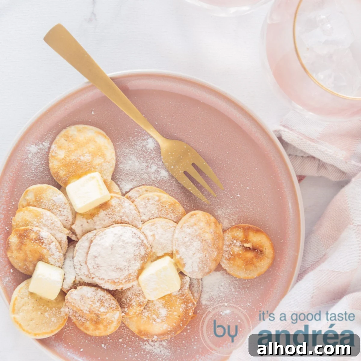 Poffertjes Dutch Mini Pancakes 6 A square photo with a pink plate with a stack of mini pancakes, butter and icing sugar, a gold fork and a white background