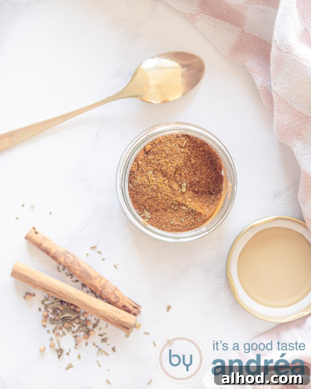A photo from above of a glass jar filled with spices. Cinnamon and dried parsley is in the front left. A golden spoon lies above it, inviting you to taste the homemade shawarma spice blend.