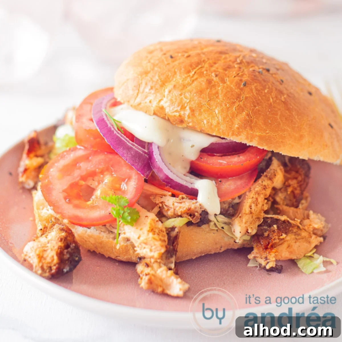 Perfect Homemade Chicken Doner Kebab 6 A Turkish sandwich with Döner chicken, tomato and lettuce and garlic sauce. A pink plate and a white background.