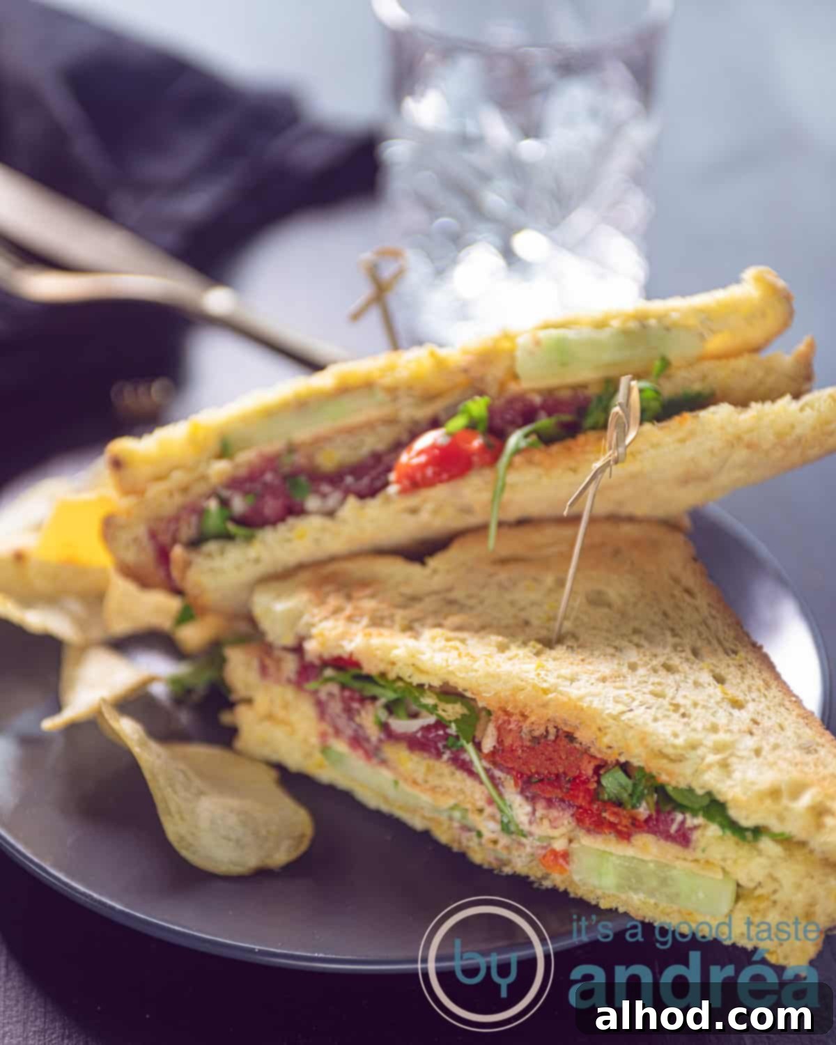 Gourmet Carpaccio Sandwich 5 An elevation photo with two half club sandwiches filled with vegetables, carpaccio, and aged cheese. A gray board and a gray background.