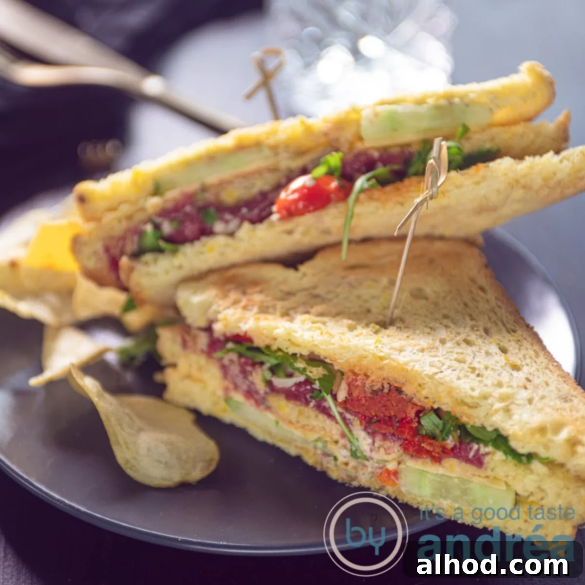 Gourmet Carpaccio Sandwich 6 A square photo with two triangles of a club sandwich with carpaccio, cheese and vegetables on a gray background.