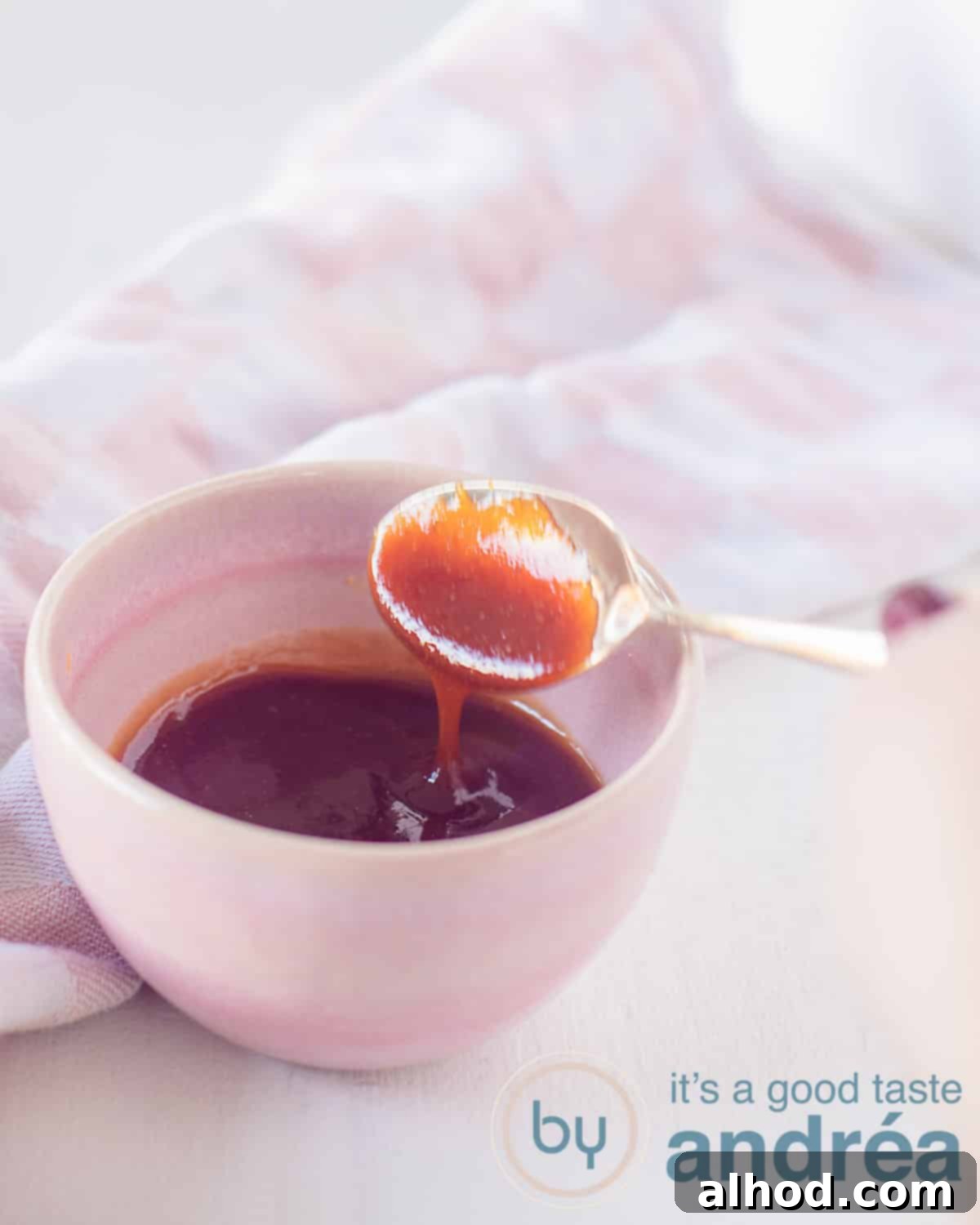 Whip Up Your Own Tonkatsu Sauce 2 A height shot of a pink bowl filled with tonkatsu sauce. A spoon has taken a scoop. A white background with a pink and white checkered tea towel in the background.