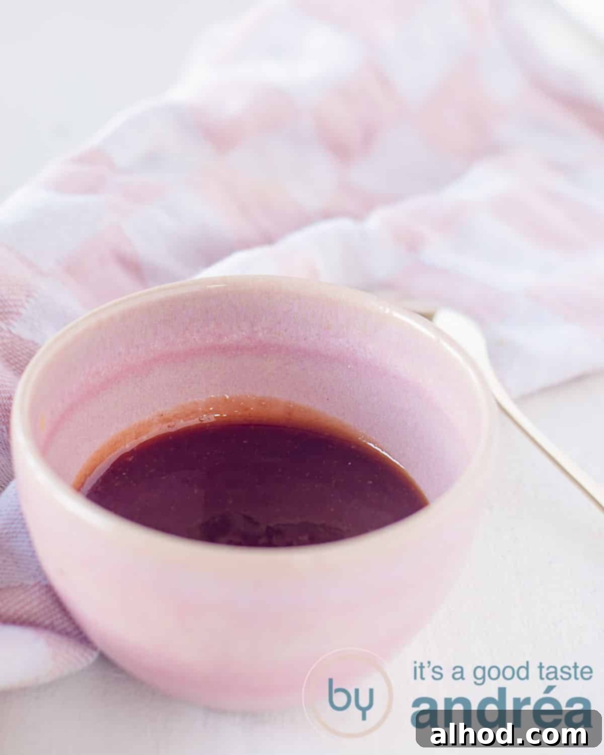 Making Delicious Tonkatsu Sauce at Home 3 An elevation photo with a pink bowl filled with Japanese sauce, tonkatsu, a golden spoon on the right, a white background. In the background a pink and white tea towel.