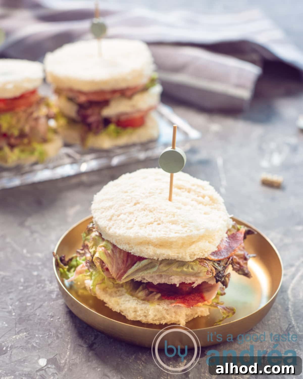 BLT Club Bites 2 A photo in the height of a bowl of gold with a bacon lettuce and tomato sandwich. On a grey background More sandwiches in the back.