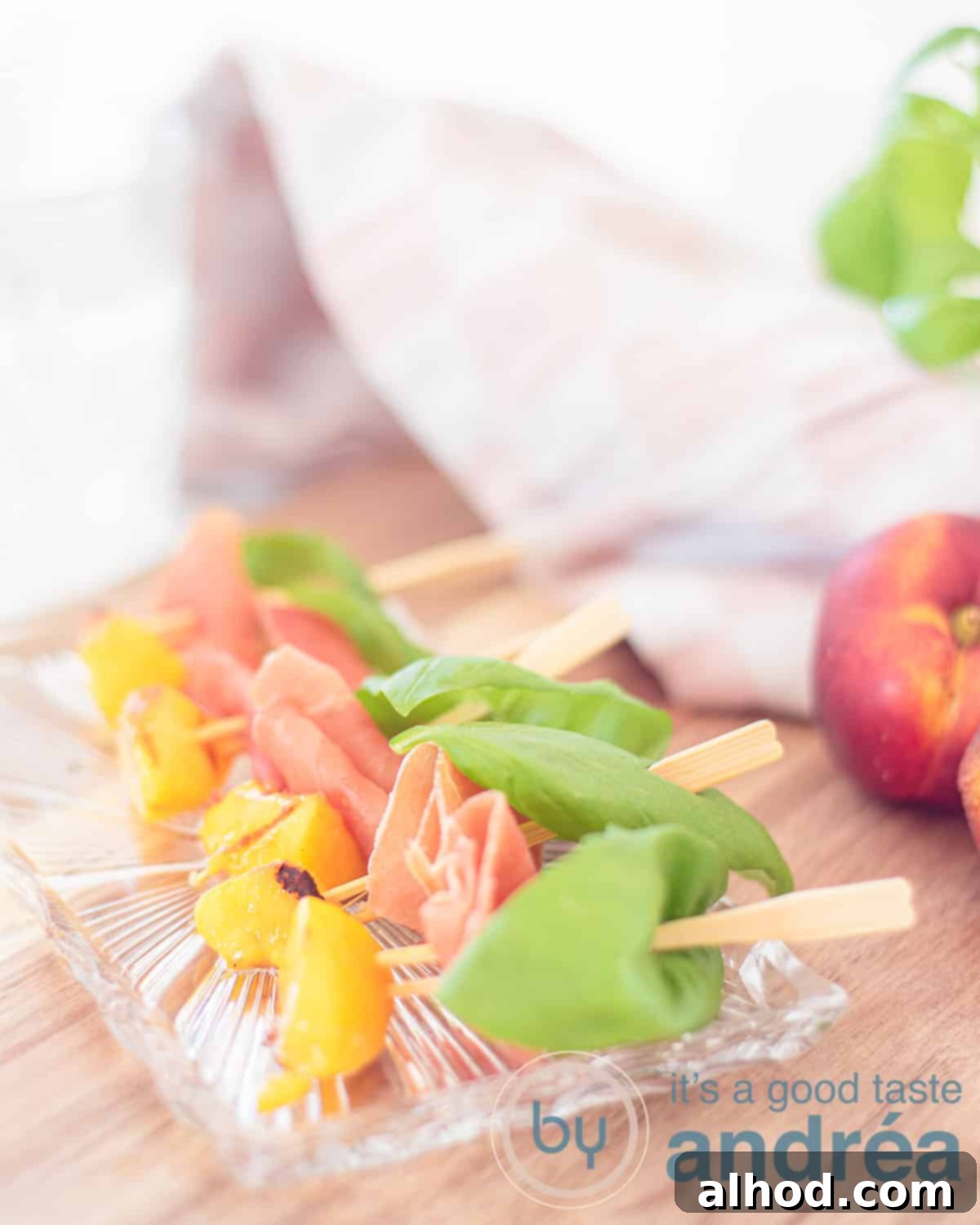 Serrano Ham Wrapped Grilled Peaches 2 A glass dish with peach snacks with ham, beautifully arranged. A pink and white tea towel is in the background, adding a touch of summer elegance to the scene.