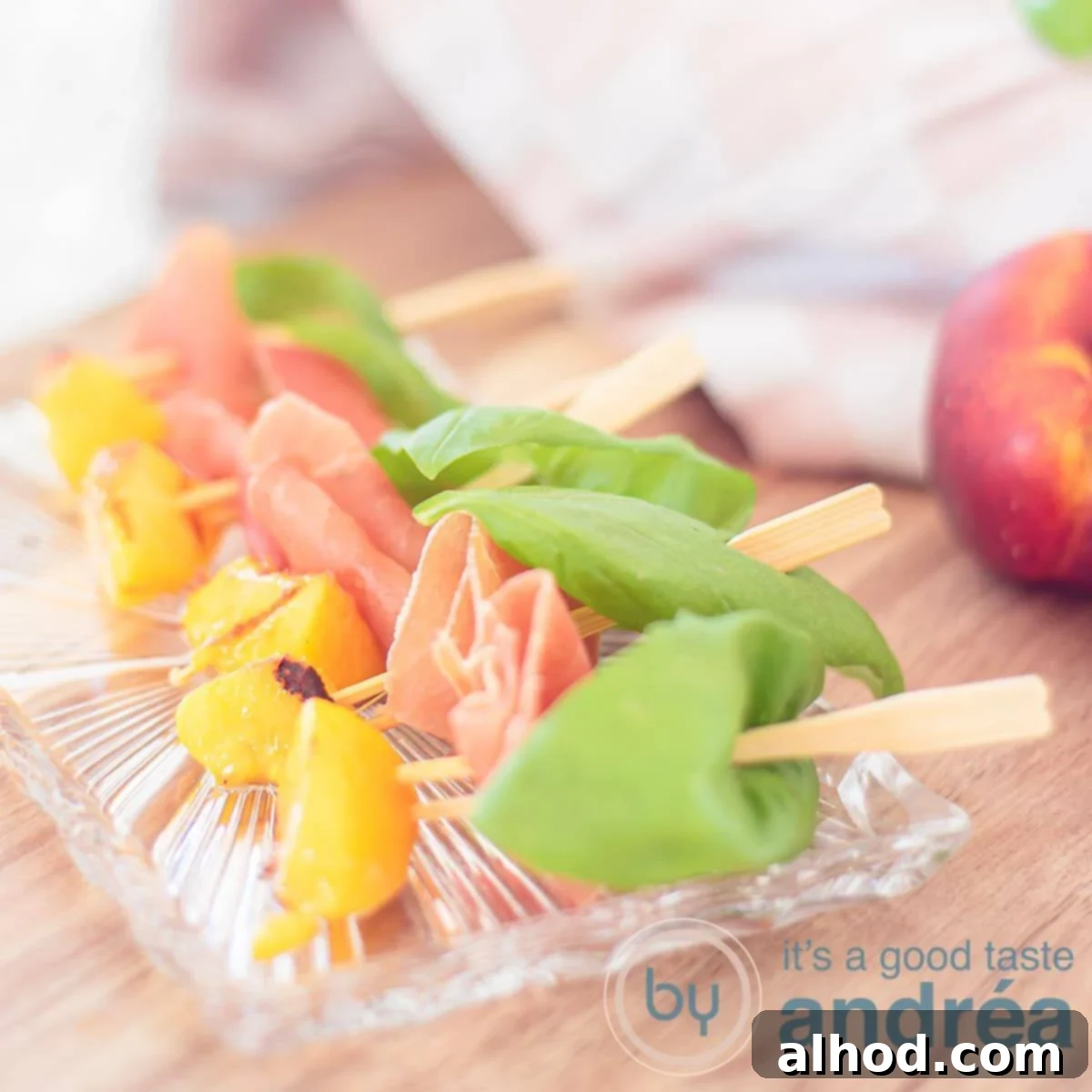 A square photo with a glass dish with tapas sticks featuring grilled peach, ham, and basil on a wooden background, ready to be served.