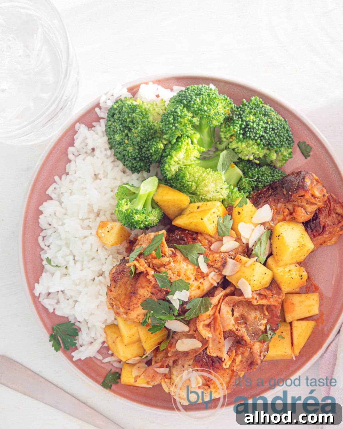 Mango-Glazed Chicken Drumsticks with Bacon 5 A photo from above with a pink plate and a white background. On the plate are two drumsticks with mango and sauce, broccoli, slivered almonds and rice.