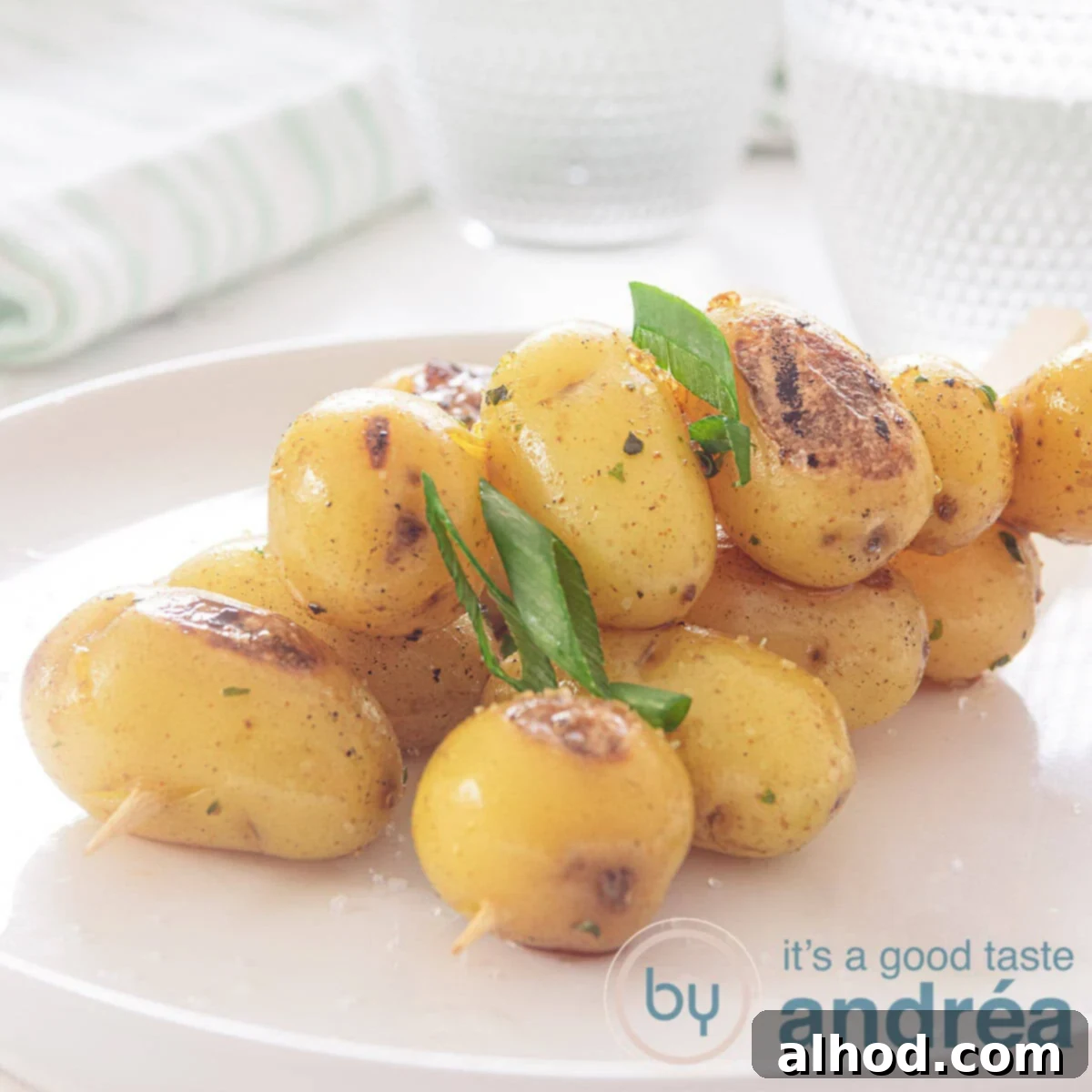 A square photo with a white plate with three baby potatoes skewers with spring onions. A white background