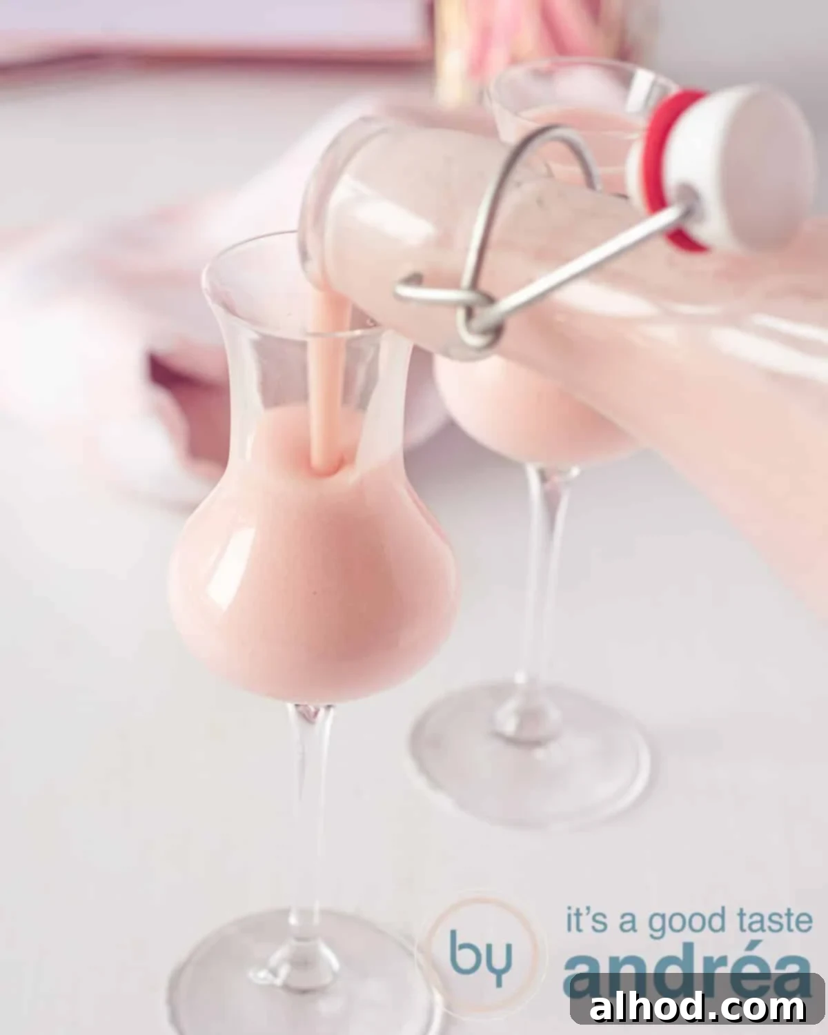 Velvet Strawberry Liqueur 2 Two cocktail glasses slanted behind each other on a white background. The front glass is filled from a bottle with strawberry cream liqueur.