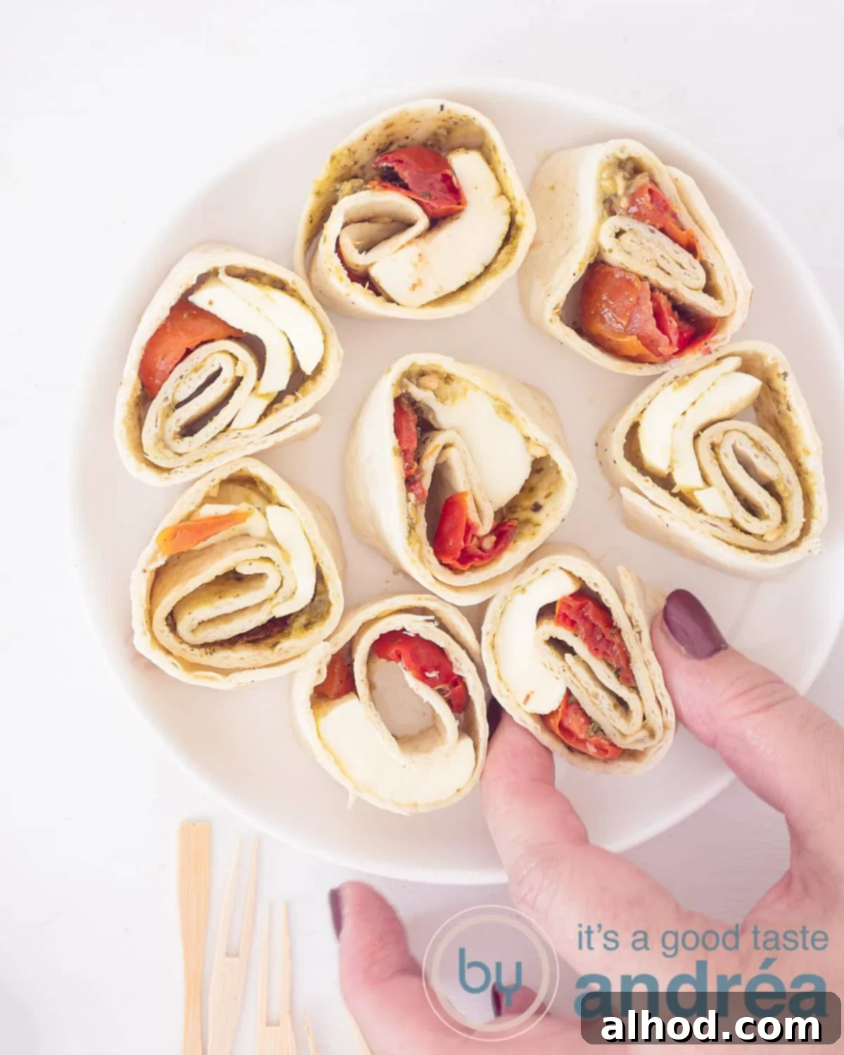 Caprese Swirls 2 A photo from above showing eight caprese wraps filled with tomato, mozzarella and basil. A hand takes a bite. A white background.