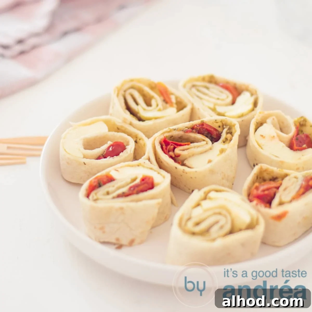Caprese Swirls 6 A square photo with a round white plate filled with 8 caprese wrap snacks. A white background. In the background a pink and white tea towel.