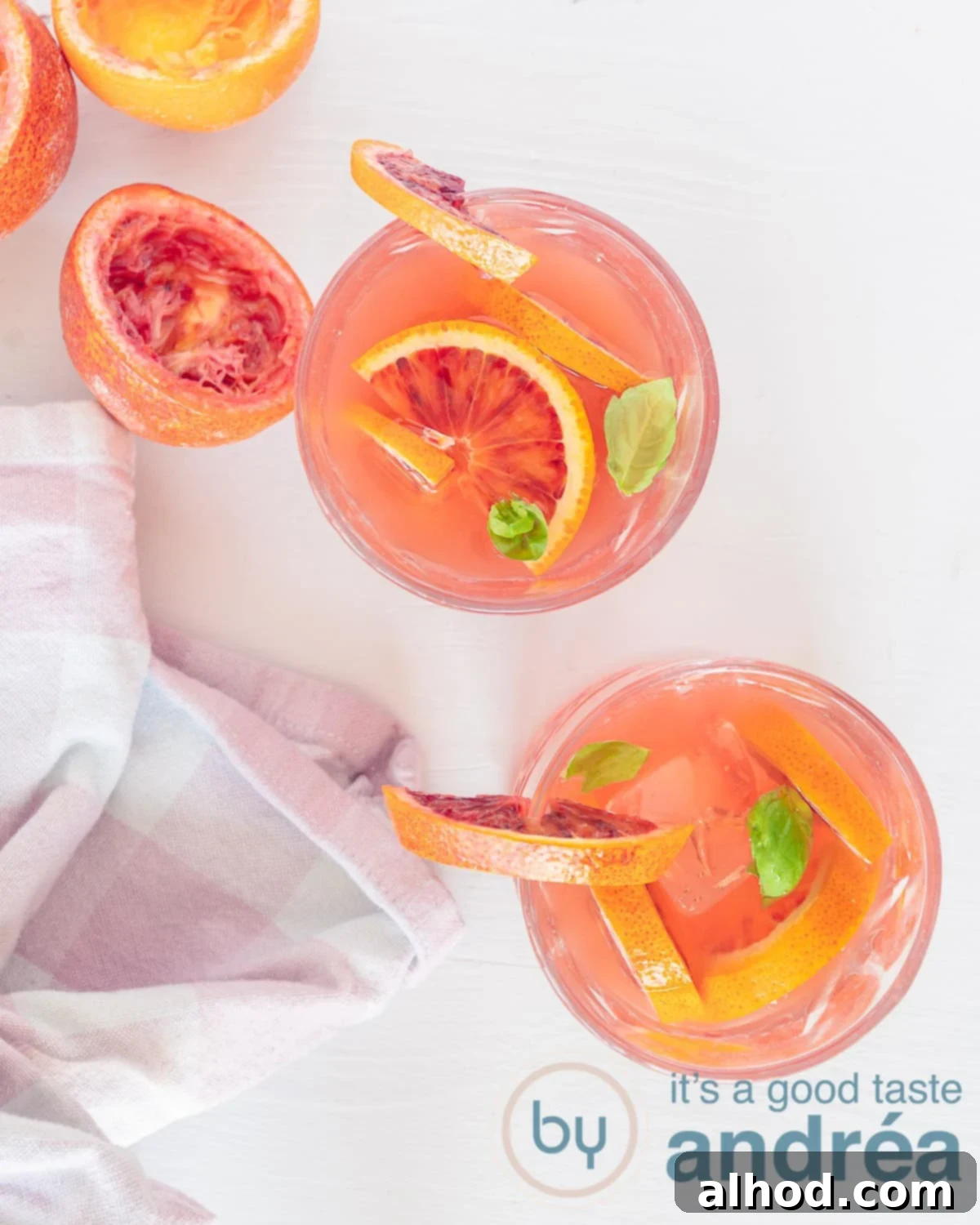 Zesty Blood Orange Iced Tea 2 A photo from above of two glasses of iced tea with blood orange and mint. A white background. At the bottom left a pink white tea towel. Squeezed halves of blood orange at the top left.
