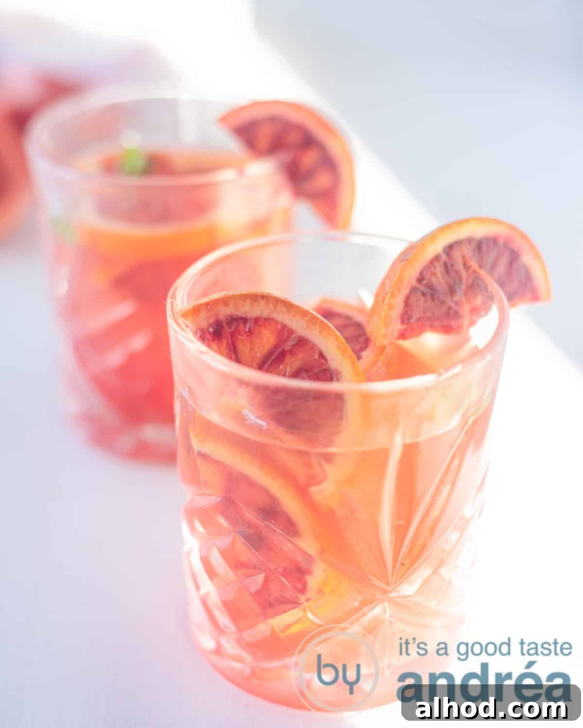 Crimson Citrus Chill 5 An elevation photo with two glasses filled with iced blood orange tea slanted one behind the other on a white background