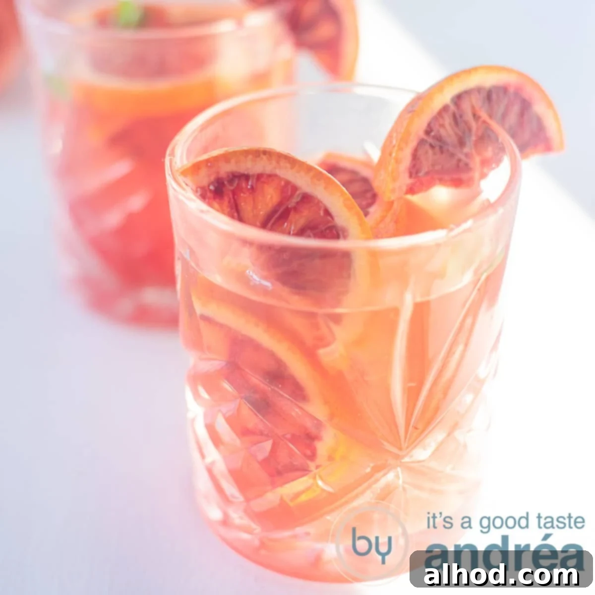 Zesty Blood Orange Iced Tea 6 A square photo with two glasses filled with blood orange iced tea, orange slices and ice on a white background