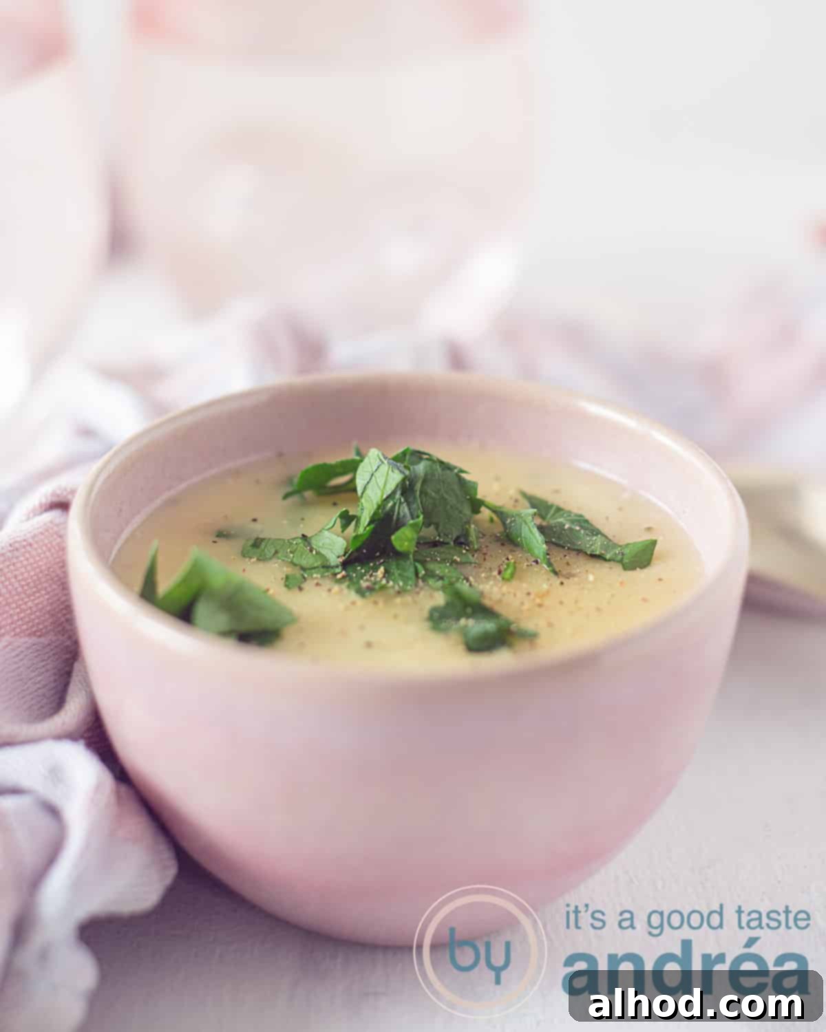 The Ultimate Garlic Parmesan Sauce 2 A height photo of a pink container with cheese sauce with parmesan, garlic and parsley. In the background a pink white tea towel and two pink glasses on a white background.