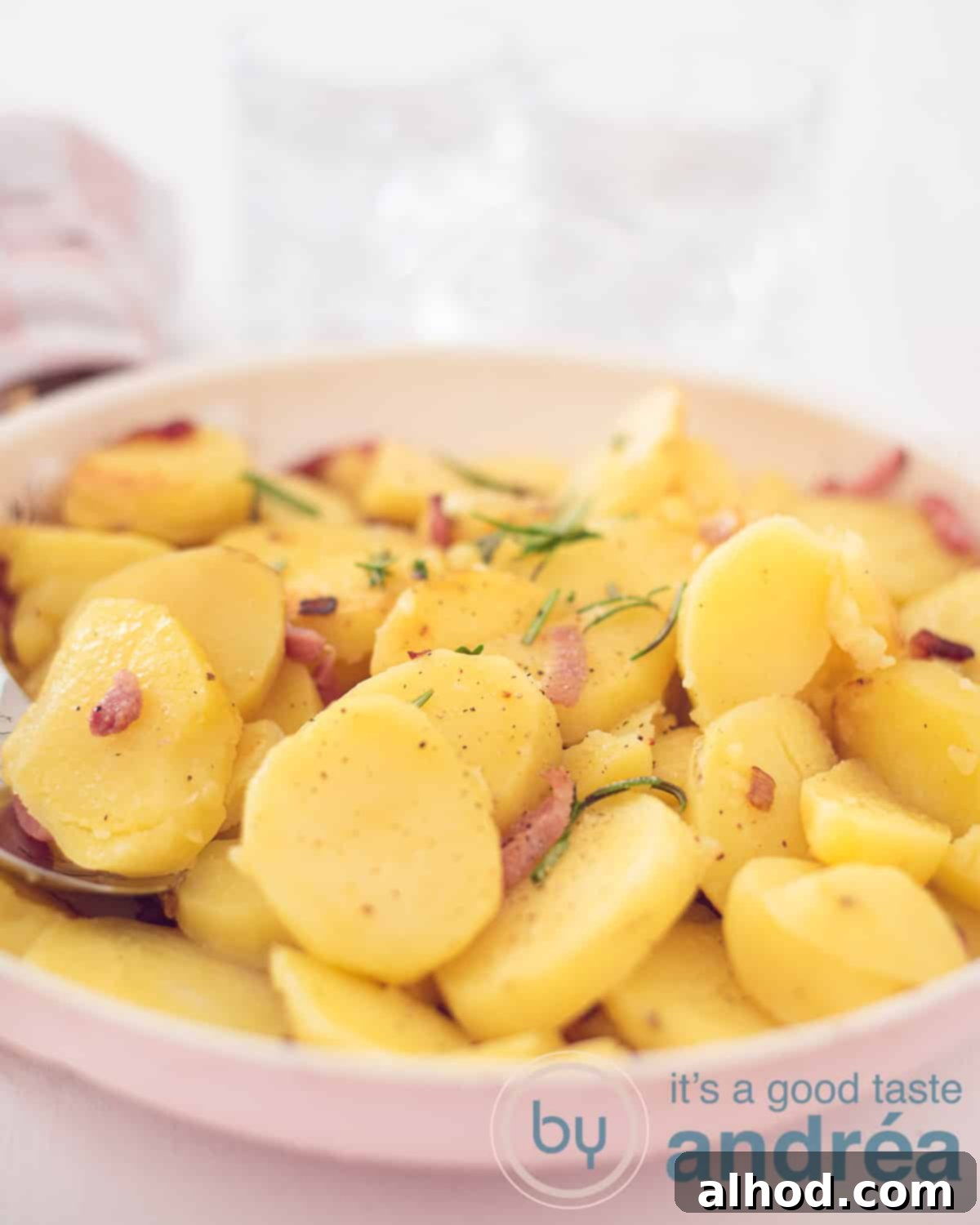 Classic German Fried Potatoes 5 An overhead photo of a pink frying pan with fried potatoes with bacon, rosemary and onion. A white background.