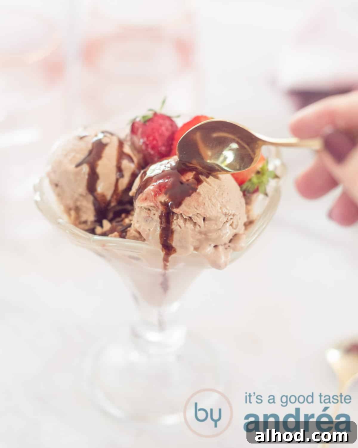 Chocolate Strawberry Froyo Treat 5 A height photo with a glass coupe filled with three scoops of chocolate Greek yogurt ice cream, garnished with fresh strawberries. A golden spoon is taking a bite. The background is white.