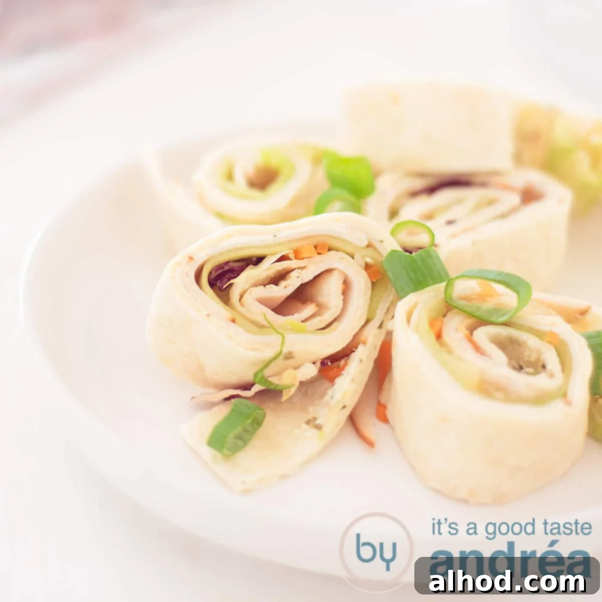 Creamy Chicken Tortilla Roll-Ups 6 A square photo with a white plate filled with round tortilla wrap snacks filled with chicken breast, herb cream cheese, cucumber and lettuce. A white background.