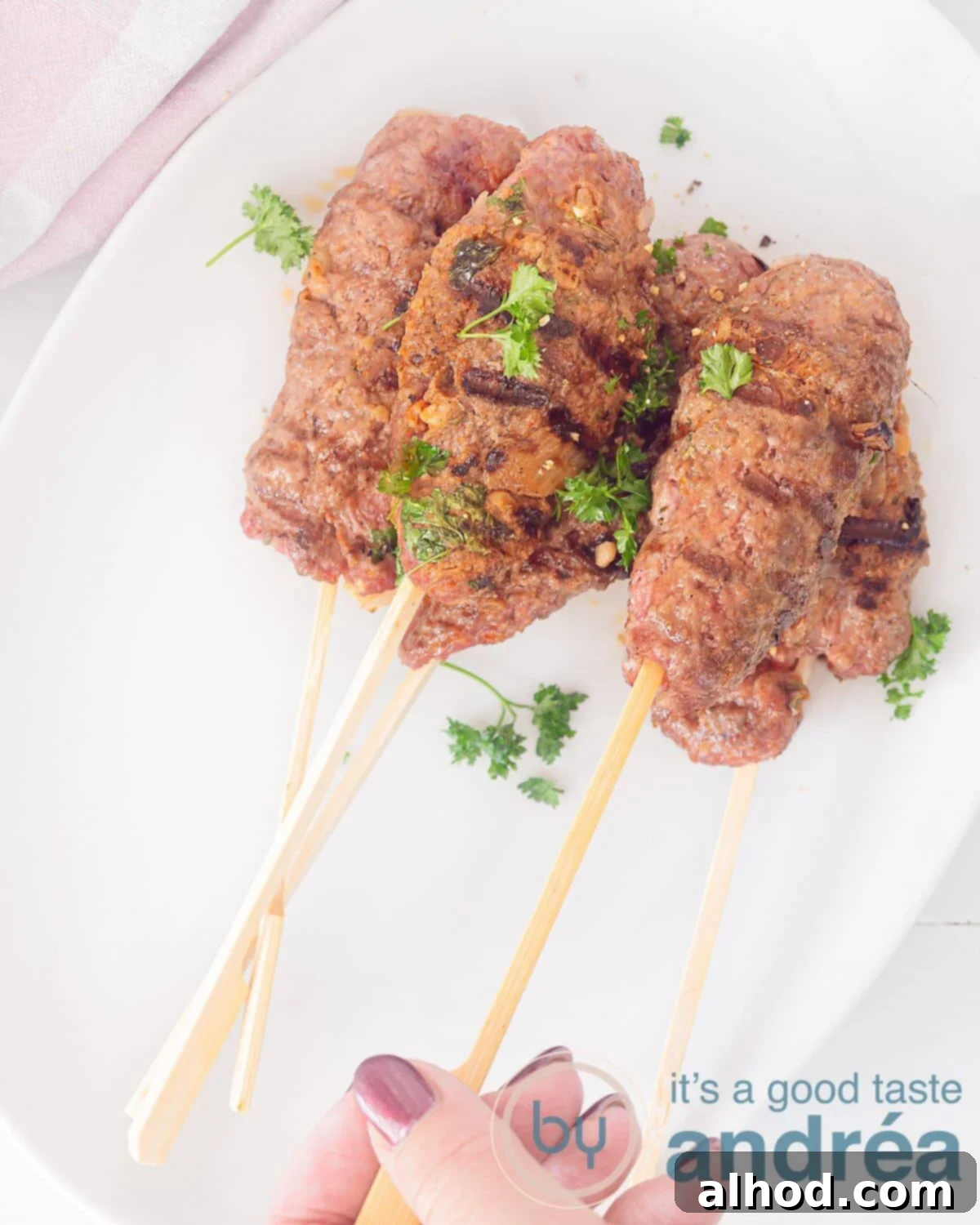 Authentic Moroccan Köfte Kebabs 3 A photo from above with skewers of köfte kebab. A hand takes a skewer. On a white dish.