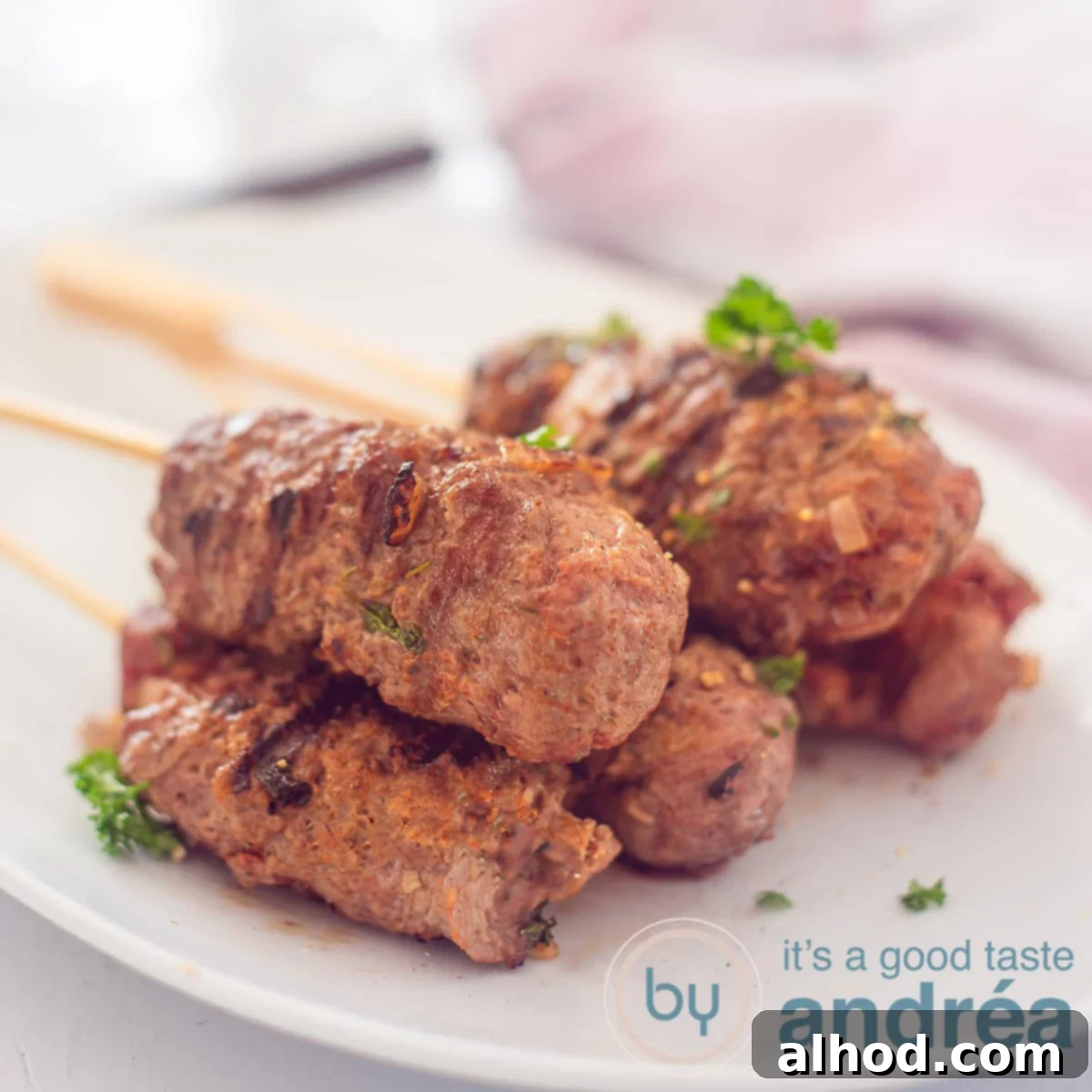 A square photo with five skewers of kefta kebab on a white dish. A white background.