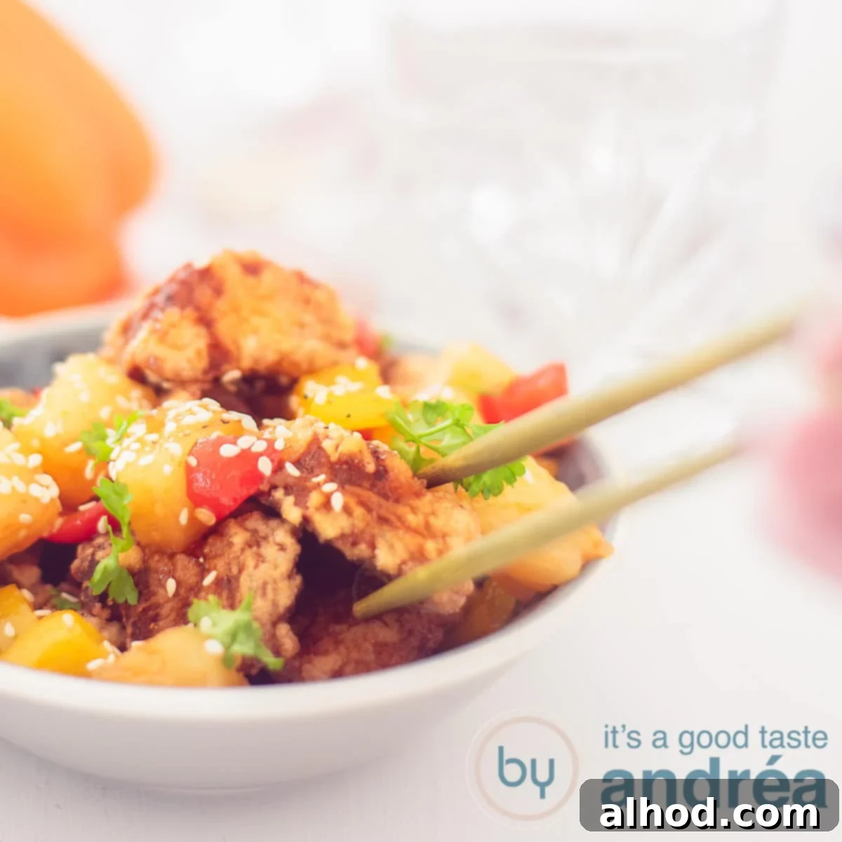 Sweet and Sour Pork 6 A square photo with a gray dish filled with crispy pork tenderloin in a sweet and sour sauce. Two chopsticks grab a block of meat