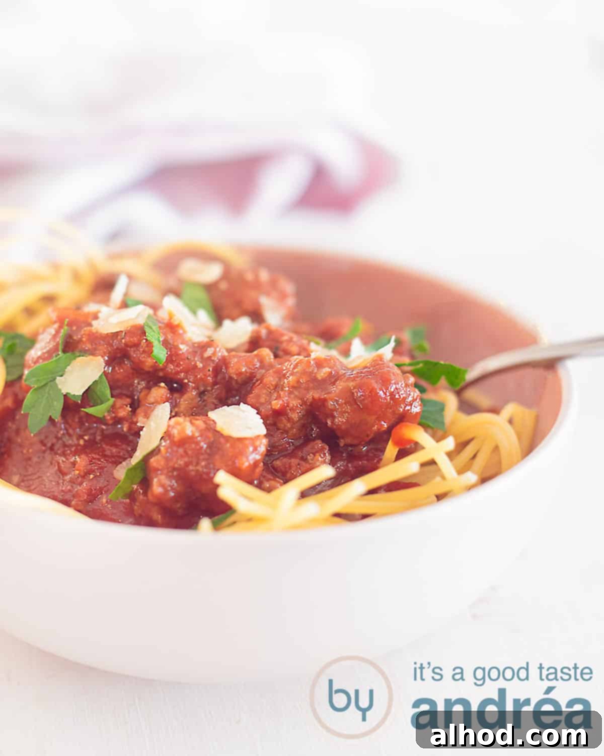 Italian Ragù alla Bolognese 5 A height shot with a pink bowl filled with spaghetti topped with classic bolognese sauce. A white background. In the background a pink tea towel